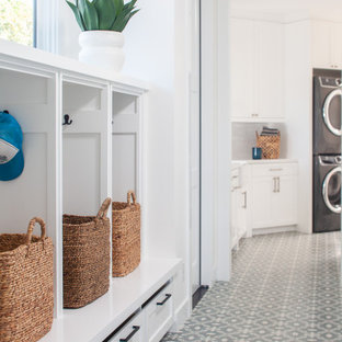 オレンジカウンティの大きいビーチスタイルのおしゃれな家事室 (シェーカースタイル扉のキャビネット、白いキャビネット、クオーツストーンカウンター、白い壁、コンクリートの床、上下配置の洗濯機・乾燥機、青い床、白いキッチンカウンター) の写真