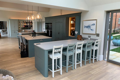 This is an example of a large traditional u-shaped open plan kitchen in Cambridgeshire with an integrated sink, shaker cabinets, green cabinets, quartz worktops, black appliances, light hardwood flooring, an island, grey worktops and feature lighting.