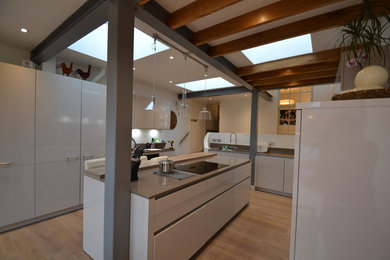 Cette photo montre une petite cuisine ouverte tendance avec un placard à porte plane, des portes de placard blanches, un sol en bois brun et îlot.