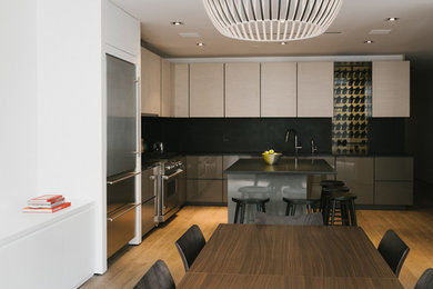 This is an example of a large contemporary u-shaped eat-in kitchen in New York with flat-panel cabinets, light wood cabinets, black splashback, stainless steel appliances, light hardwood floors and with island.