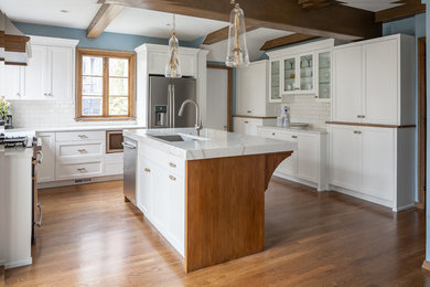 Example of a mid-sized tuscan u-shaped medium tone wood floor eat-in kitchen design in Other with an undermount sink, shaker cabinets, white cabinets, quartzite countertops, white backsplash, ceramic backsplash, white appliances, an island and white countertops