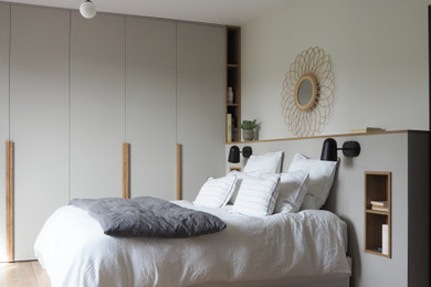 Cette photo montre une chambre parentale tendance de taille moyenne avec un mur blanc, un sol en bois brun et un sol beige.