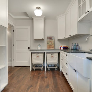 ミネアポリスの大きいトランジショナルスタイルのおしゃれな洗濯室 (エプロンフロントシンク、落し込みパネル扉のキャビネット、白いキャビネット、ソープストーンカウンター、グレーの壁、濃色無垢フローリング、上下配置の洗濯機・乾燥機、茶色い床) の写真