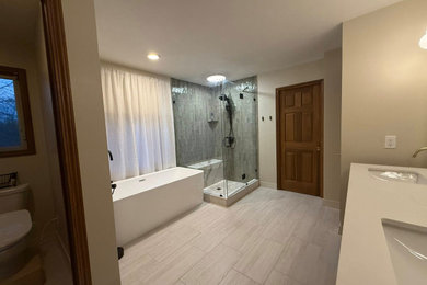 Example of a mid-sized minimalist master green tile and porcelain tile porcelain tile, gray floor and double-sink bathroom design in Grand Rapids with shaker cabinets, medium tone wood cabinets, a bidet, beige walls, an undermount sink, granite countertops, a hinged shower door, beige countertops and a freestanding vanity