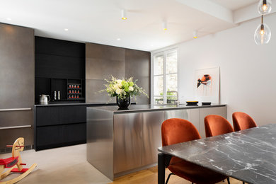 This is an example of a large modern galley open plan kitchen in Paris with stainless steel cabinets, stainless steel benchtops and with island.