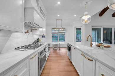 Open concept kitchen - large transitional galley light wood floor, brown floor and vaulted ceiling open concept kitchen idea in Austin with an undermount sink, recessed-panel cabinets, white cabinets, quartzite countertops, white backsplash, marble backsplash, stainless steel appliances, an island and white countertops
