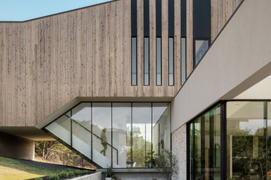 Réalisation d'une grande façade de maison minimaliste en bois à niveaux décalés avec un toit plat et un toit mixte.