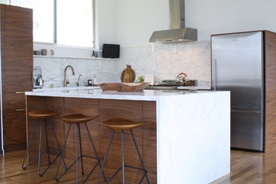 Photo of a contemporary l-shaped open plan kitchen in Los Angeles with flat-panel cabinets, medium wood cabinets, white splashback, stainless steel appliances, light hardwood floors, with island, marble benchtops, a single-bowl sink and marble splashback.