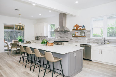 Example of a large transitional l-shaped vinyl floor and brown floor open concept kitchen design in Tampa with an undermount sink, shaker cabinets, white cabinets, quartz countertops, gray backsplash, ceramic backsplash, stainless steel appliances, an island and white countertops