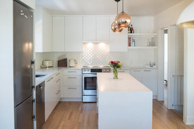 Inspiration for a mid-sized transitional l-shaped light wood floor eat-in kitchen remodel in Vancouver with an undermount sink, flat-panel cabinets, white cabinets, quartz countertops, white backsplash, ceramic backsplash, stainless steel appliances and an island