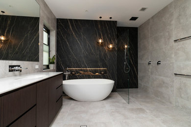 Photo of an expansive modern 3/4 bathroom in Sydney with flat-panel cabinets, dark wood cabinets, a freestanding tub, an open shower, a wall-mount toilet, gray tile, porcelain tile, multi-coloured walls, porcelain floors, an undermount sink, tile benchtops, grey floor, an open shower and white benchtops.
