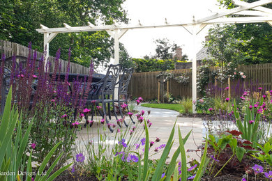 Ejemplo de jardín tradicional de tamaño medio en patio trasero con pérgola, exposición total al sol, adoquines de piedra natural y con madera