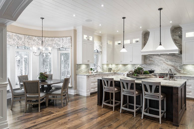 This is an example of a beach style l-shaped eat-in kitchen in Toronto with an undermount sink, recessed-panel cabinets, white cabinets, multi-coloured splashback, stone slab splashback, stainless steel appliances, dark hardwood floors, with island, brown floor and multi-coloured benchtop.