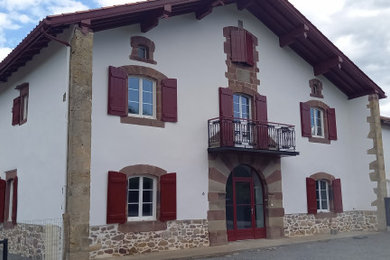 Cette photo montre une façade de maison blanche chic à deux étages et plus avec un toit à deux pans, un toit en tuile et un toit rouge.