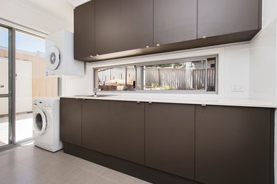 Design ideas for a mid-sized contemporary single-wall dedicated laundry room in Perth with a drop-in sink, flat-panel cabinets, brown cabinets, solid surface benchtops, white walls and a stacked washer and dryer.