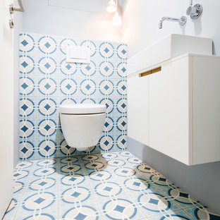 Ejemplo de aseo actual, pequeño, con armarios con paneles lisos, puertas de armario blancas, sanitario de dos piezas, baldosas y/o azulejos azules, baldosas y/o azulejos blancos, baldosas y/o azulejos de cemento, paredes grises, suelo de azulejos de cemento, lavabo sobreencimera y suelo multicolor