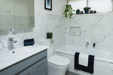 This is an example of a modern bathroom in Melbourne with shaker cabinets, grey cabinets, a drop-in tub, black and white tile, porcelain tile, white walls, porcelain floors, solid surface benchtops, grey floor, white benchtops, a niche, a single vanity and a freestanding vanity.