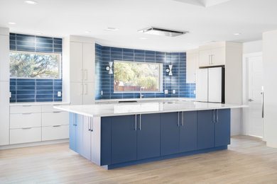 Example of a minimalist laminate floor and beige floor kitchen pantry design in Austin with flat-panel cabinets, blue cabinets, quartz countertops, blue backsplash, ceramic backsplash, white appliances, an island and white countertops