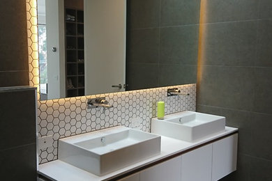 This is an example of a mid-sized contemporary master bathroom in Other with flat-panel cabinets, white cabinets, an open shower, a one-piece toilet, gray tile, porcelain tile, grey walls, porcelain floors, a vessel sink, engineered quartz benchtops, grey floor, an open shower and white benchtops.