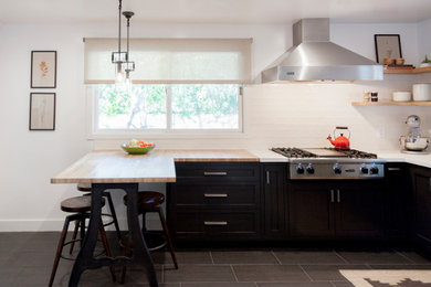 This is an example of a mid-sized contemporary u-shaped separate kitchen in Los Angeles with a farmhouse sink, shaker cabinets, black cabinets, marble benchtops, white splashback, ceramic splashback, stainless steel appliances, porcelain floors, a peninsula, grey floor and white benchtop.