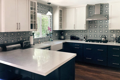 Inspiration for a mid-sized eclectic u-shaped medium tone wood floor and brown floor enclosed kitchen remodel in New York with a farmhouse sink, shaker cabinets, blue cabinets, blue backsplash, porcelain backsplash, stainless steel appliances, white countertops and no island