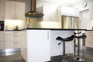 Mid-sized trendy u-shaped enclosed kitchen photo in Other with a single-bowl sink, flat-panel cabinets, white cabinets, granite countertops, black appliances and an island