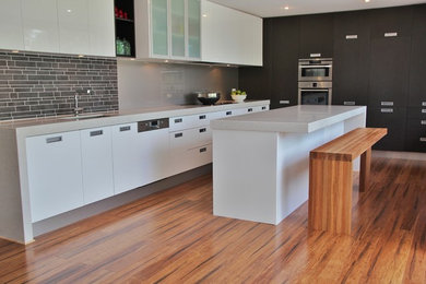 Inspiration for a large modern l-shaped open plan kitchen in Melbourne with a single-bowl sink, flat-panel cabinets, white cabinets, quartz benchtops, metallic splashback, glass sheet splashback, stainless steel appliances and with island.