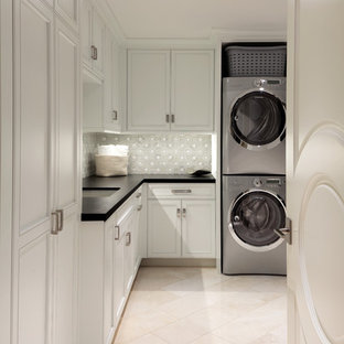 マイアミのトランジショナルスタイルのおしゃれな洗濯室 (アンダーカウンターシンク、落し込みパネル扉のキャビネット、白いキャビネット、上下配置の洗濯機・乾燥機、ベージュの床、黒いキッチンカウンター) の写真