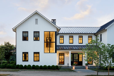 Cette photo montre une façade de maison blanche nature à un étage avec un toit à deux pans, un toit en métal et un toit noir.