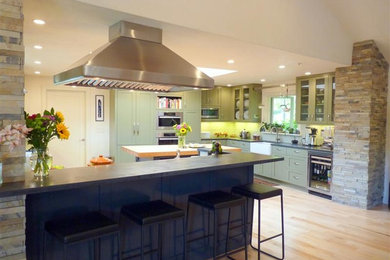 Large transitional light wood floor open concept kitchen photo in San Francisco with a farmhouse sink, shaker cabinets, green cabinets, white backsplash, glass tile backsplash, stainless steel appliances and an island