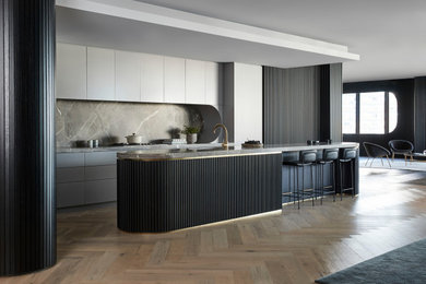 Modern galley open plan kitchen in Melbourne with a double-bowl sink, marble benchtops, grey splashback, marble splashback, black appliances, medium hardwood floors, with island, brown floor, black benchtop and wallpaper.