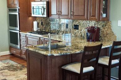 This is an example of a mid-sized transitional l-shaped eat-in kitchen in Philadelphia with an undermount sink, raised-panel cabinets, medium wood cabinets, granite benchtops, multi-coloured splashback, stone slab splashback, stainless steel appliances, medium hardwood floors and a peninsula.