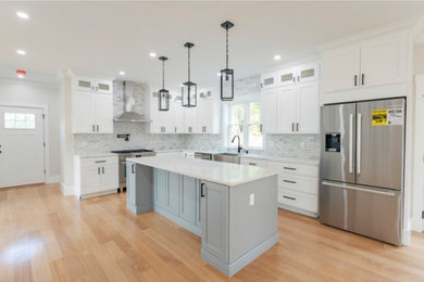 Example of a large transitional l-shaped light wood floor open concept kitchen design in Boston with a farmhouse sink, shaker cabinets, white cabinets, white backsplash, stainless steel appliances and an island