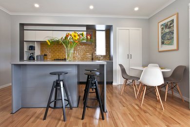 Photo of a contemporary galley eat-in kitchen in Sydney with flat-panel cabinets, grey cabinets, yellow splashback, light hardwood floors and with island.