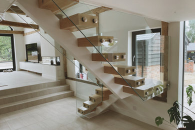 Inspiration for a modern wood l-shaped glass railing staircase in Essex with wood risers and a feature wall.