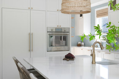 Large beach style l-shaped light wood floor open concept kitchen photo in Vancouver with an undermount sink, shaker cabinets, white cabinets, quartz countertops, blue backsplash, ceramic backsplash, paneled appliances, an island and white countertops