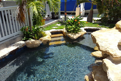 Small tropical backyard custom-shaped natural pool in Miami with natural stone pavers and a water feature.