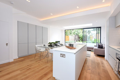This is an example of a large modern grey and white kitchen/diner in London with an integrated sink, flat-panel cabinets, grey cabinets, composite countertops, white splashback, ceramic splashback, integrated appliances, medium hardwood flooring, an island, white worktops, a coffered ceiling and feature lighting.