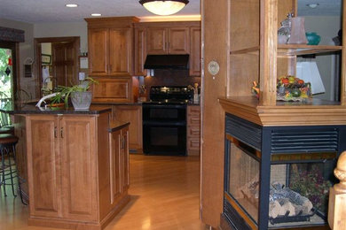 Transitional medium tone wood floor eat-in kitchen photo in Other with raised-panel cabinets, medium tone wood cabinets, granite countertops, black appliances and an island