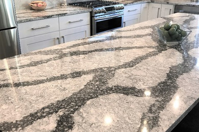 Example of a large transitional l-shaped medium tone wood floor and gray floor eat-in kitchen design in Other with an undermount sink, recessed-panel cabinets, white cabinets, quartz countertops, gray backsplash, marble backsplash, stainless steel appliances and an island