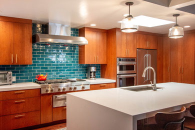 Immagine di un cucina con isola centrale moderno con ante lisce, paraspruzzi blu, paraspruzzi con piastrelle in ceramica, elettrodomestici in acciaio inossidabile e top bianco