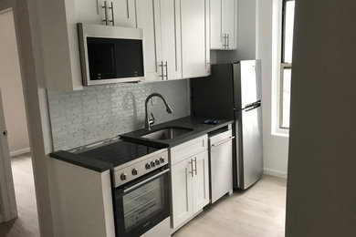 Example of a mid-sized transitional galley light wood floor and gray floor eat-in kitchen design in New York with an undermount sink, recessed-panel cabinets, white cabinets, quartz countertops, gray backsplash, matchstick tile backsplash, stainless steel appliances, a peninsula and gray countertops