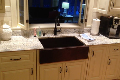 Inspiration for a contemporary medium tone wood floor kitchen remodel in Boston with a farmhouse sink, recessed-panel cabinets, beige cabinets, granite countertops, white backsplash, stone tile backsplash, stainless steel appliances and an island