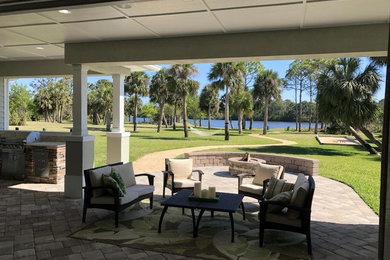 Patio - large tropical backyard concrete paver patio idea in Orlando with a fire pit and a roof extension