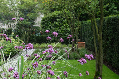 Mittelgroßer, Halbschattiger Moderner Garten im Sommer, neben dem Haus mit Blumenbeet, Natursteinplatten und Metallzaun in Bonn
