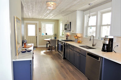 Photo of a mid-sized country galley eat-in kitchen in Other with a single-bowl sink, shaker cabinets, blue cabinets, quartz benchtops, white splashback, subway tile splashback, stainless steel appliances, medium hardwood floors, brown floor and white benchtop.