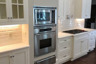 This is an example of a large traditional galley kitchen pantry in Atlanta with an undermount sink, white cabinets, onyx benchtops, white splashback, ceramic splashback, white appliances, dark hardwood floors, a peninsula, brown floor, white benchtop and beaded inset cabinets.