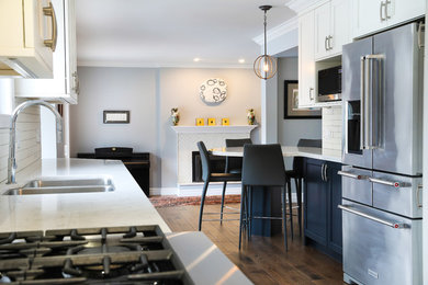 Design ideas for a mid-sized transitional galley eat-in kitchen in Toronto with an undermount sink, beaded inset cabinets, blue cabinets, quartz benchtops, white splashback, ceramic splashback, stainless steel appliances, medium hardwood floors, a peninsula, brown floor and white benchtop.