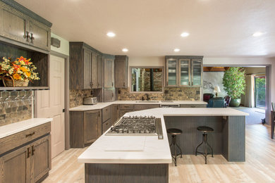 This is an example of a large transitional u-shaped kitchen in San Francisco with a single-bowl sink, shaker cabinets, grey cabinets, multi-coloured splashback, stone tile splashback, stainless steel appliances, with island and brown floor.