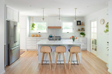 Inspiration for a transitional l-shaped light wood floor and beige floor kitchen remodel in Raleigh with white cabinets, white backsplash, stainless steel appliances, white countertops, a farmhouse sink and an island